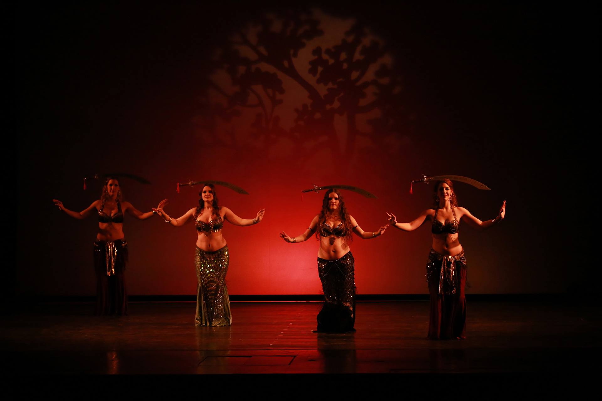 Vier Tänzerinnen in glitzernden Kostümen führen eine beeindruckende FatChance Bellydance-Choreografie mit Schwertern auf dem Kopf im Tanzstudio in München auf.