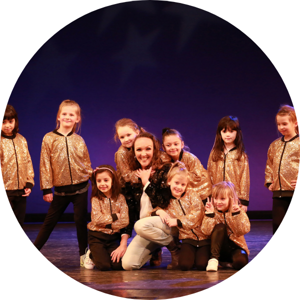 Hip-Hop-Lehrerin sitzt mit einer Gruppe tanzender Kinder in goldenen Jacken auf der Bühne bei KayJay’s in München