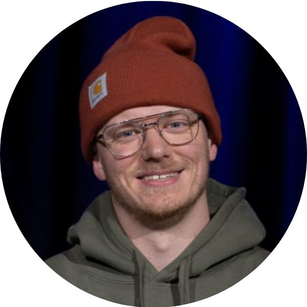 Portrait von Paul „Paulito“ Westerhoff, Breakdance-Trainer bei KayJay’s in München, orange Beanie und Brille, lächelnd vor dunklem Hintergrund.