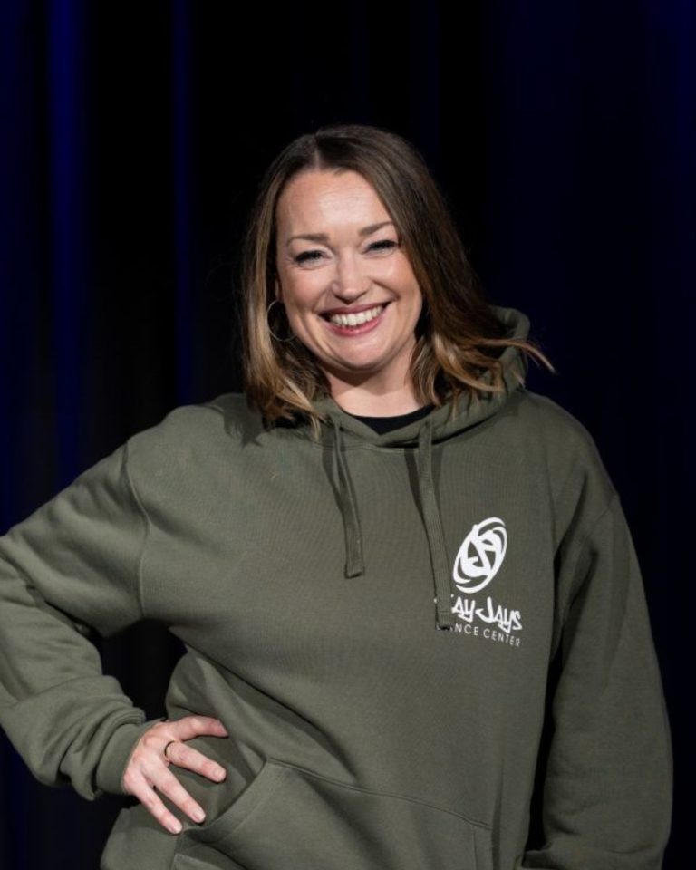 Leonie, Trainerin bei KayJays, im olivgrünen KayJays-Hoodie vor blauem Bühnenvorhang