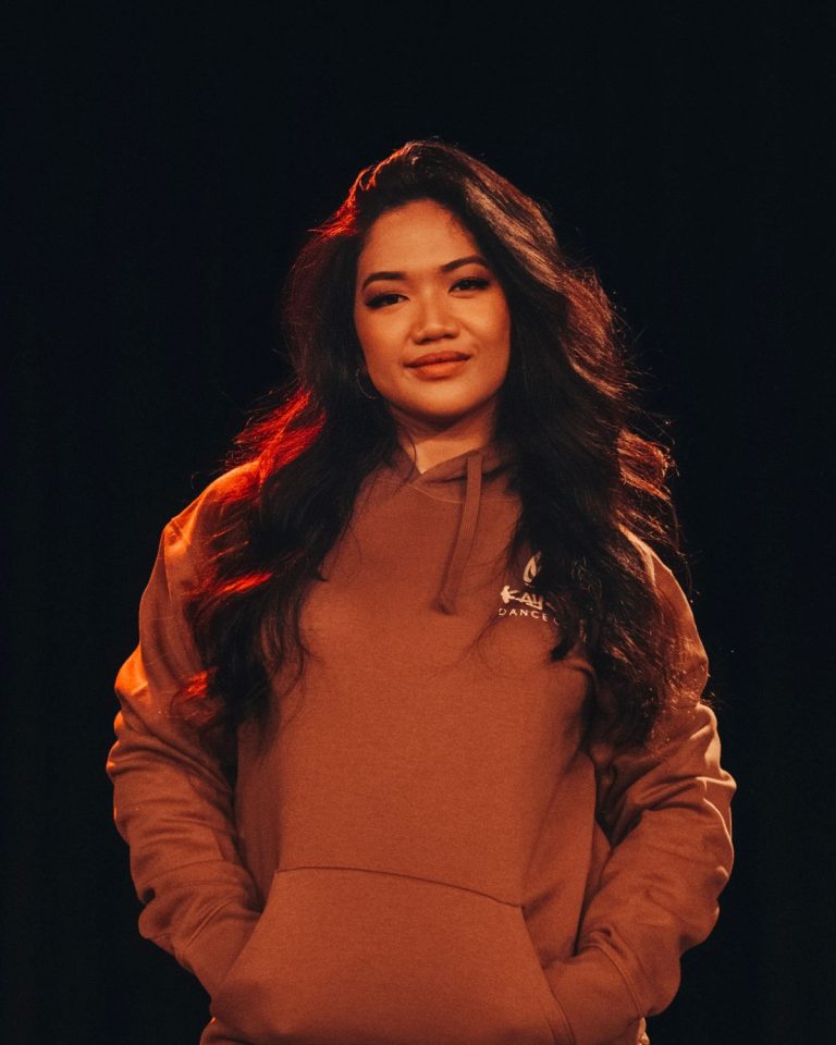 Putri, Trainerin bei KayJays, im rostbraunen KayJays-Hoodie im warmen Bühnenlicht